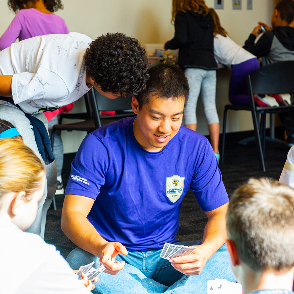 A male camp couselor playing cards with children campers.