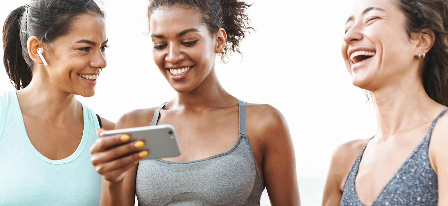 Three young woman smiling. One is holding a cellphone.