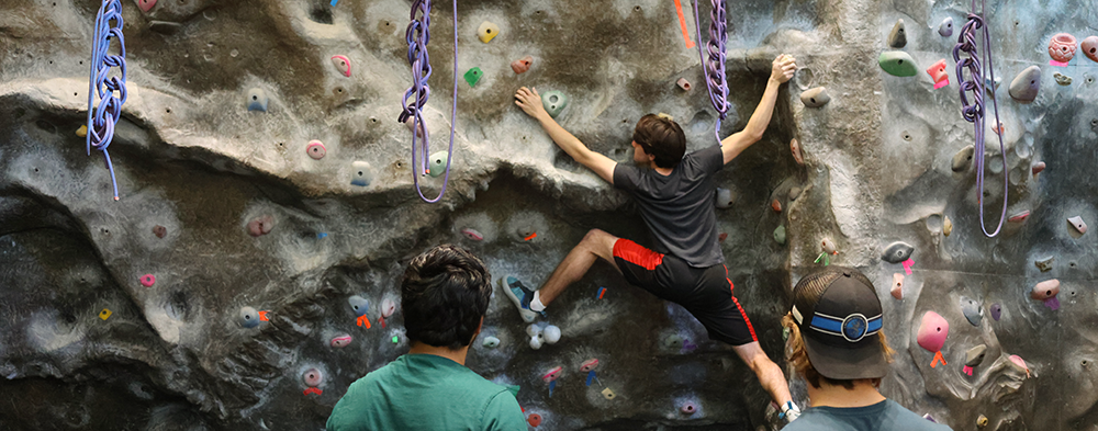 A guy climbs the wall while 2 others are watching.