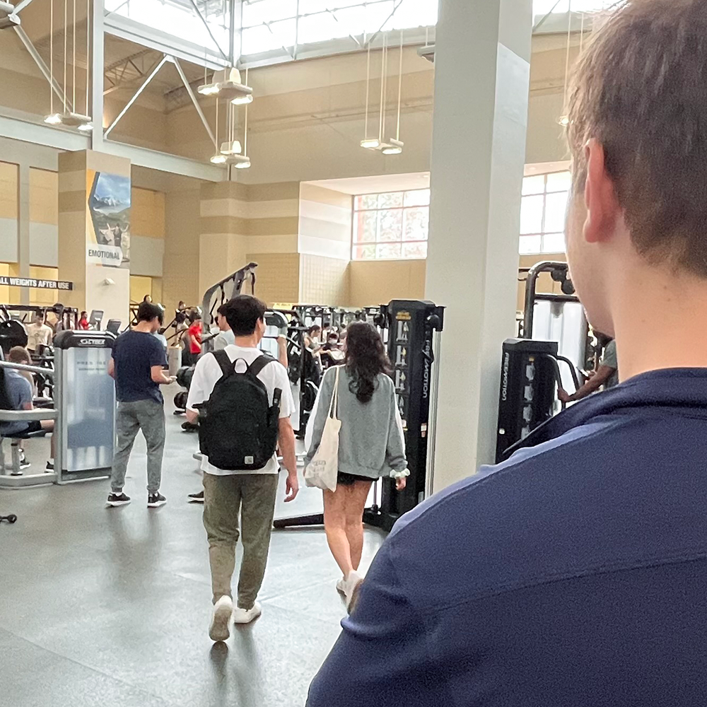 The profile of a guy looking at students walking by at the fitness area.